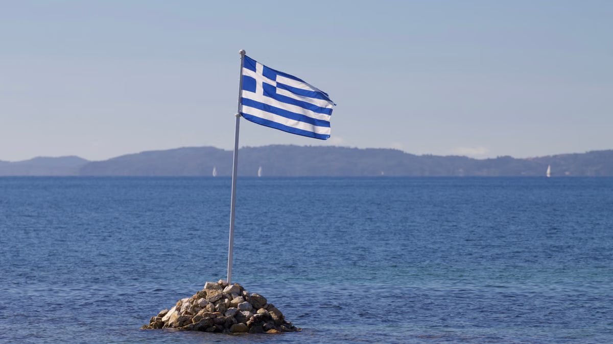 Greek flag waves over rocky island with serene Ionian Sea backdrop in Corfu, Greece.